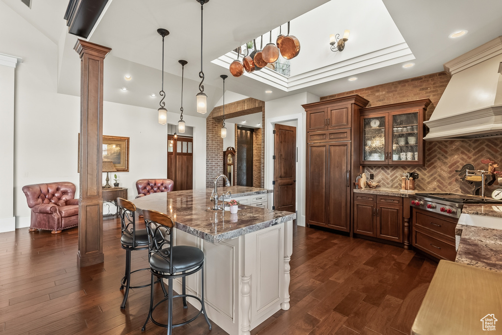 Kitchen with decorative light fixtures, decorative columns, dark hardwood / wood-style floors, tasteful backsplash, and custom exhaust hood