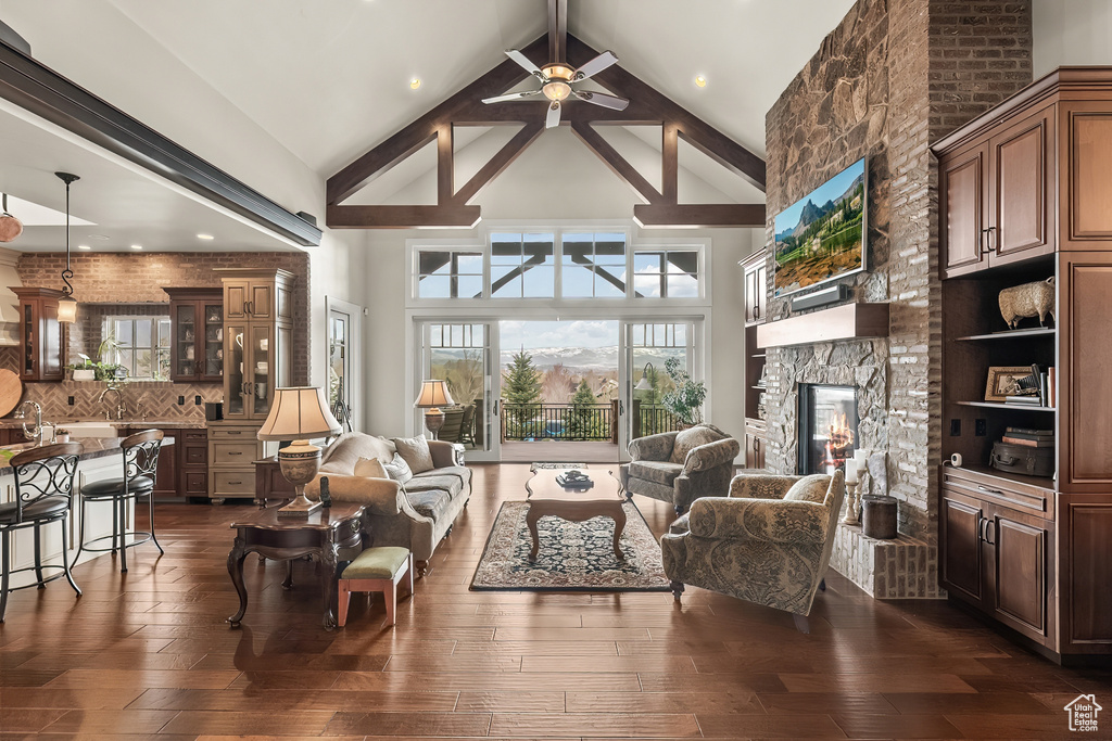Living room featuring high vaulted ceiling, beam ceiling, ceiling fan, and a stone fireplace