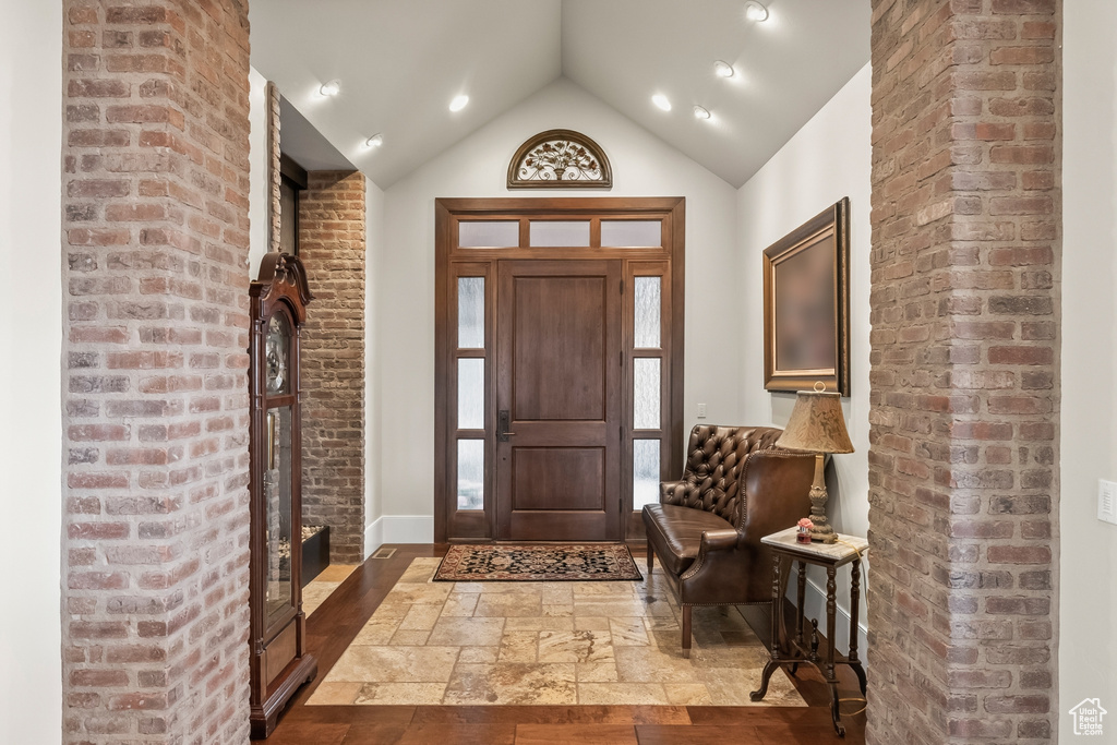 Tiled entrance foyer featuring lofted ceiling and brick wall