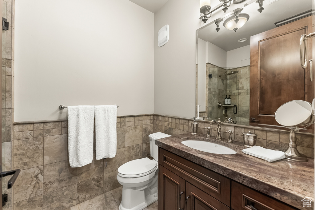 Bathroom with tile walls, toilet, vanity with extensive cabinet space, tile flooring, and tasteful backsplash
