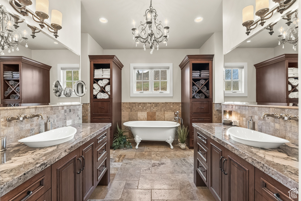 Bathroom with dual bowl vanity, a bath to relax in, tile walls, backsplash, and tile flooring