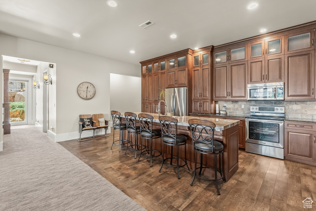 Kitchen featuring light stone counters, hardwood / wood-style floors, stainless steel appliances, and a kitchen island with sink