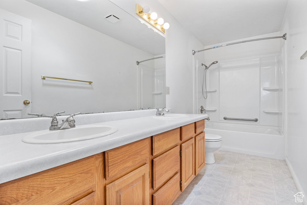 Full bathroom with shower / bathtub combination, tile floors, large vanity, dual sinks, and toilet