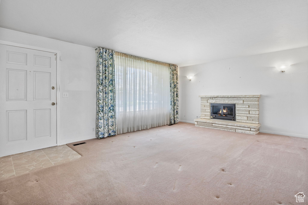 Unfurnished living room with a stone fireplace and carpet floors
