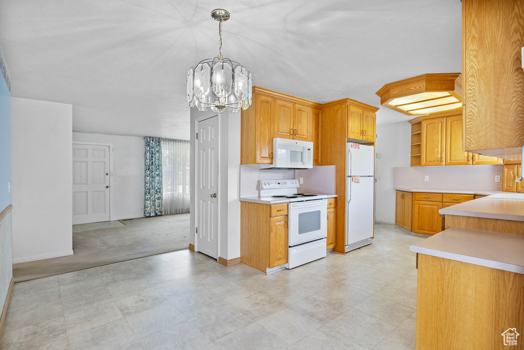 Kitchen with light colored carpet, decorative light fixtures, white appliances, sink, and an inviting chandelier