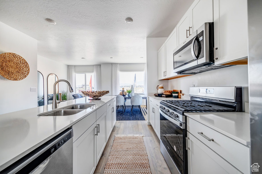 Kitchen featuring appliances with stainless steel finishes, light hardwood / wood-style floors, white cabinets, and sink