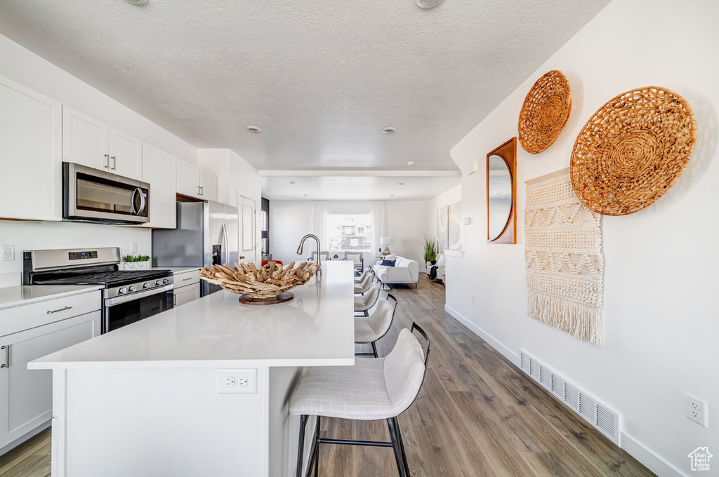 Kitchen with a textured ceiling, stainless steel appliances, hardwood / wood-style floors, and an island with sink
