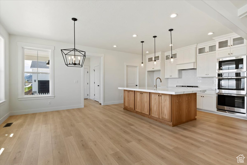 Kitchen with decorative light fixtures, stainless steel appliances, light hardwood / wood-style floors, tasteful backsplash, and a kitchen island with sink