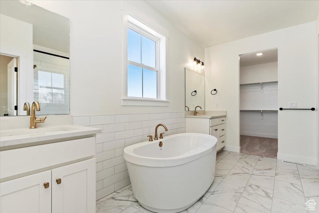 Bathroom featuring tile floors, tile walls, a tub, and dual vanity