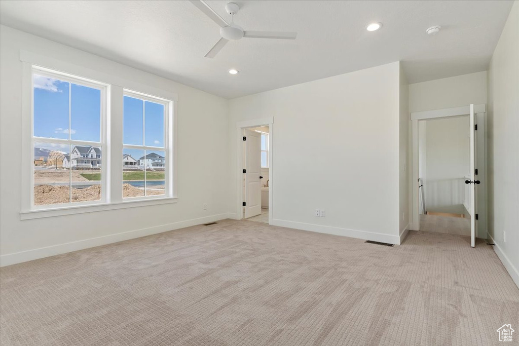 Unfurnished bedroom with connected bathroom, light carpet, and ceiling fan