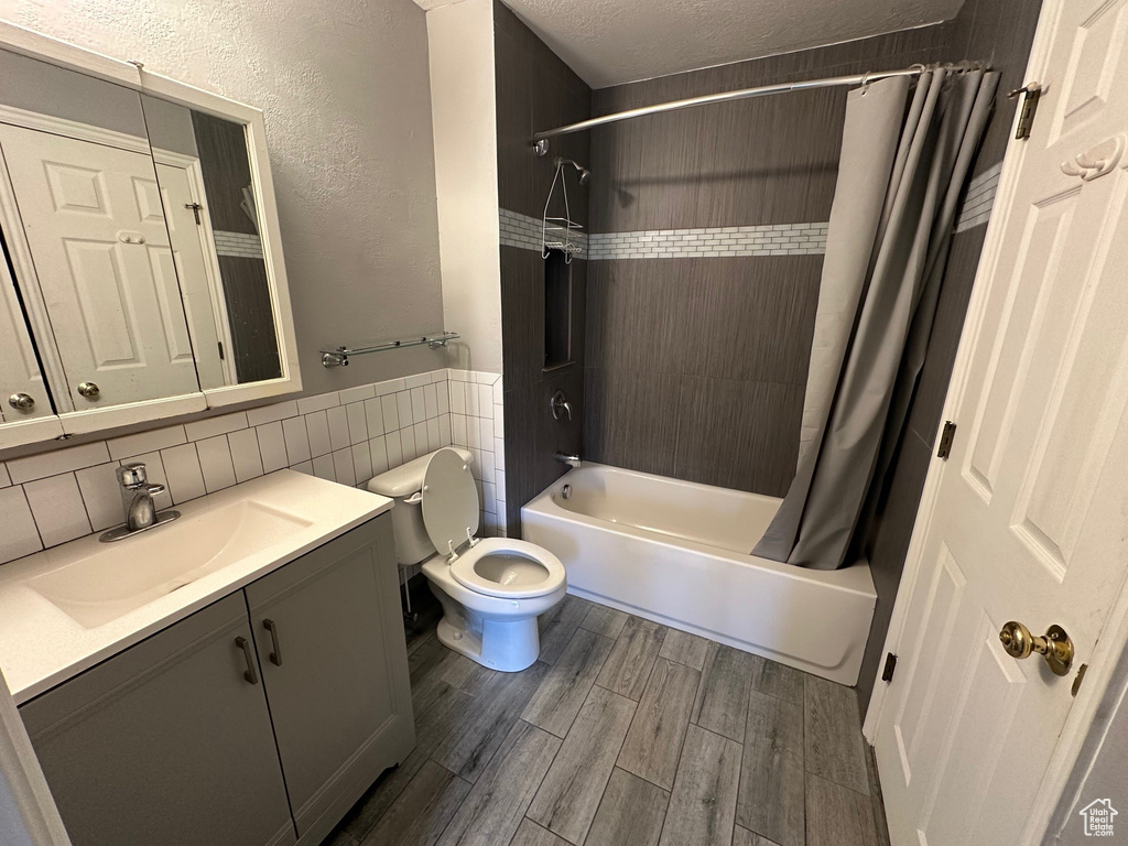 Full bathroom with oversized vanity, toilet, shower / tub combo with curtain, tasteful backsplash, and hardwood / wood-style flooring
