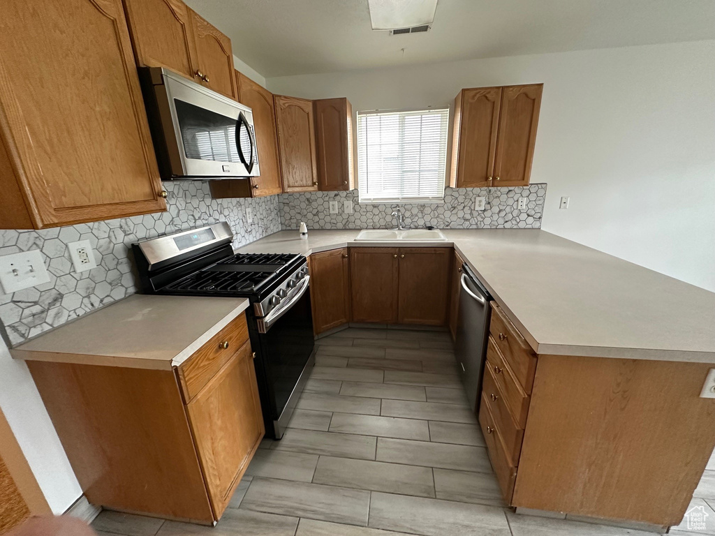 Kitchen with kitchen peninsula, backsplash, stainless steel appliances, light tile flooring, and sink