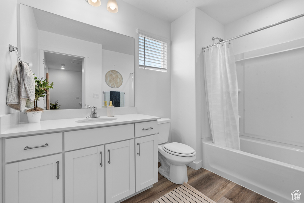 Full bathroom with hardwood / wood-style floors, vanity, shower / bathtub combination with curtain, and toilet