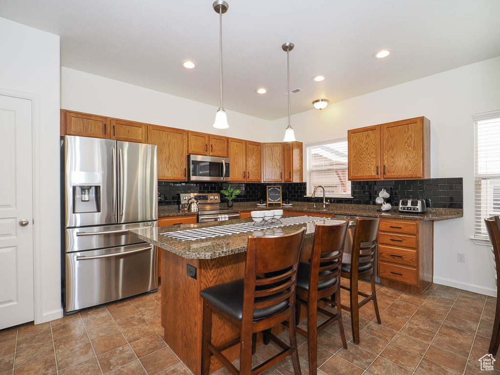 Kitchen featuring tile flooring, a kitchen island, backsplash, stainless steel appliances, and pendant lighting