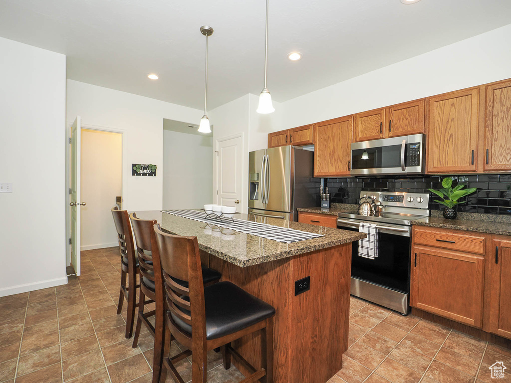 Kitchen with decorative light fixtures, appliances with stainless steel finishes, backsplash, a kitchen breakfast bar, and light tile floors