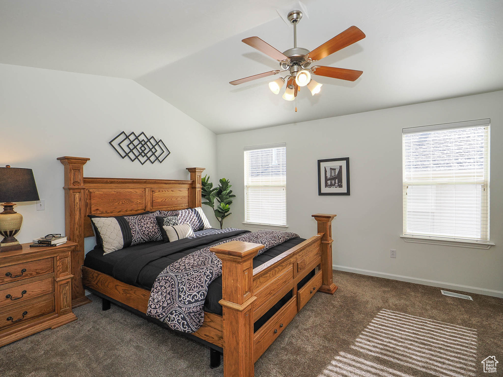 Carpeted bedroom featuring ceiling fan, vaulted ceiling, and multiple windows