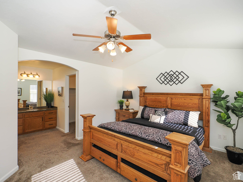 Carpeted bedroom featuring ensuite bath, ceiling fan, sink, and lofted ceiling