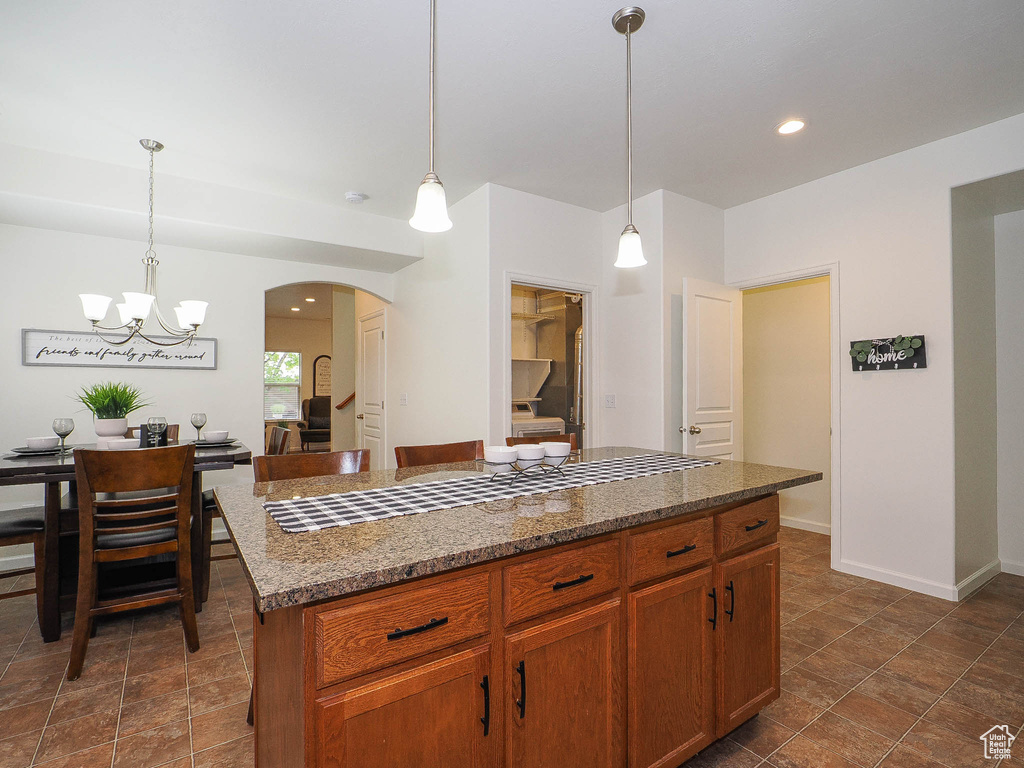 Kitchen with hanging light fixtures, dark tile floors, a center island, and an inviting chandelier
