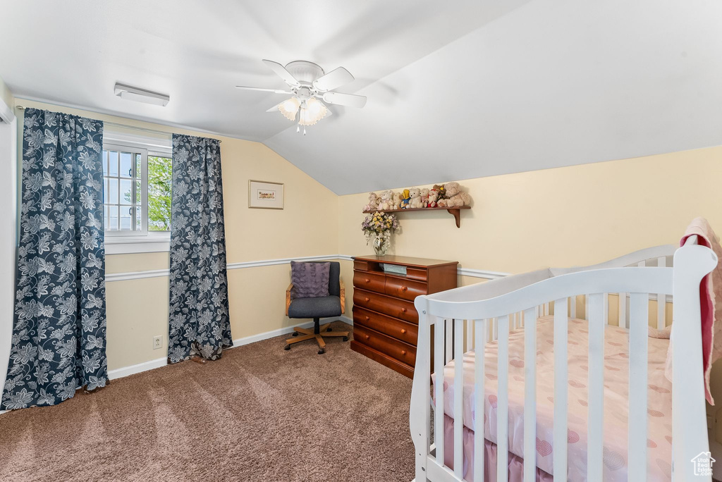 Carpeted bedroom with a nursery area, ceiling fan, and vaulted ceiling