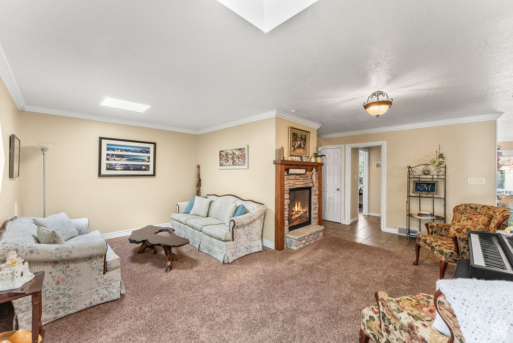 Living room featuring a textured ceiling, carpet floors, crown molding, and a stone fireplace