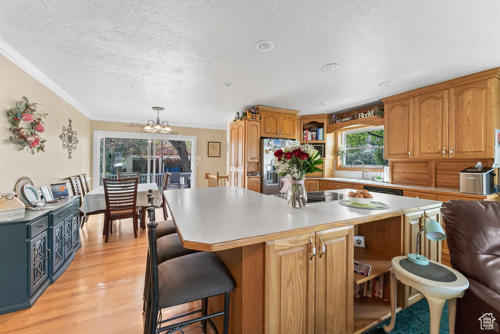 Kitchen with decorative light fixtures, a kitchen island, light hardwood / wood-style floors, stainless steel fridge, and an inviting chandelier