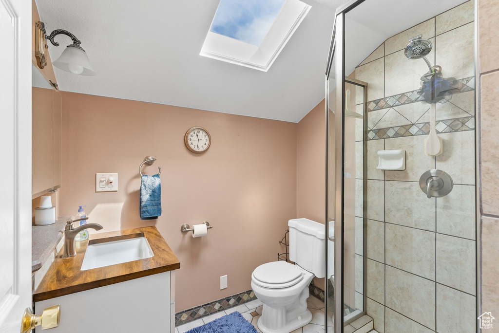 Bathroom with tile flooring, vaulted ceiling with skylight, toilet, a shower with shower door, and vanity