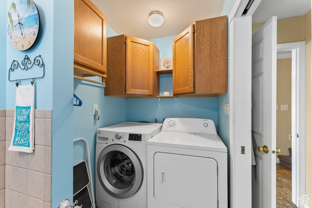 Laundry room with cabinets, light tile floors, and washing machine and clothes dryer