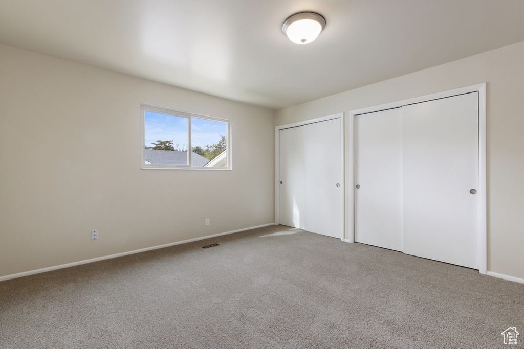 Unfurnished bedroom with carpet flooring and multiple closets