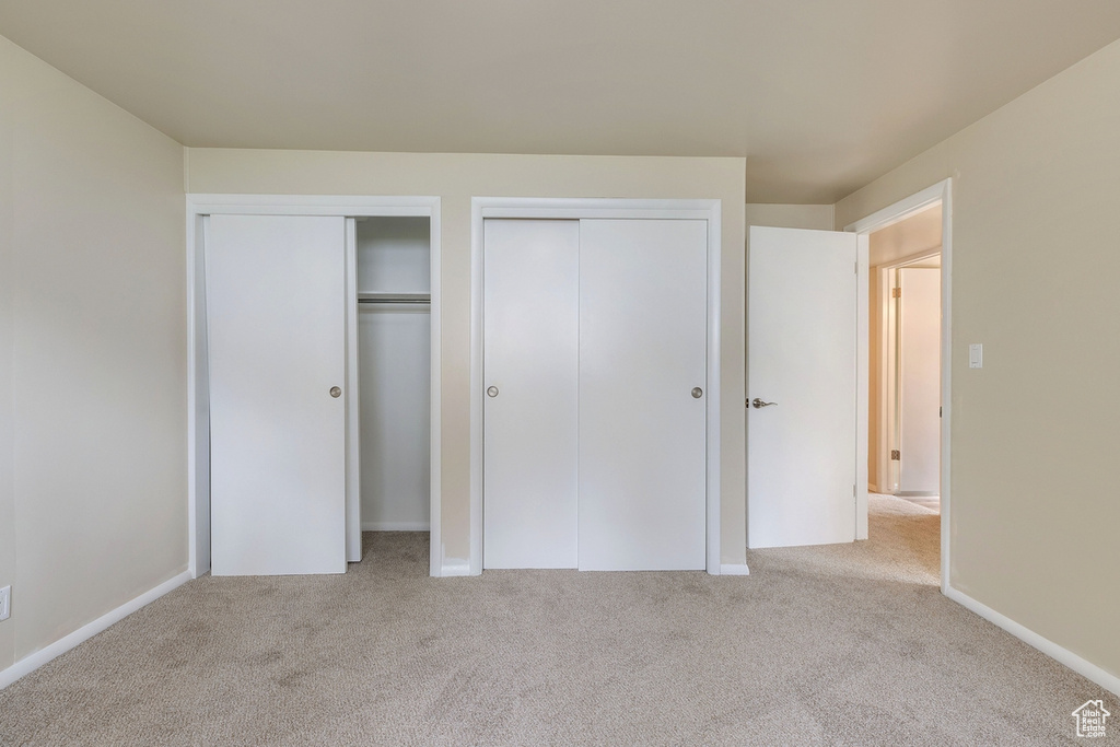 Unfurnished bedroom featuring light carpet and multiple closets