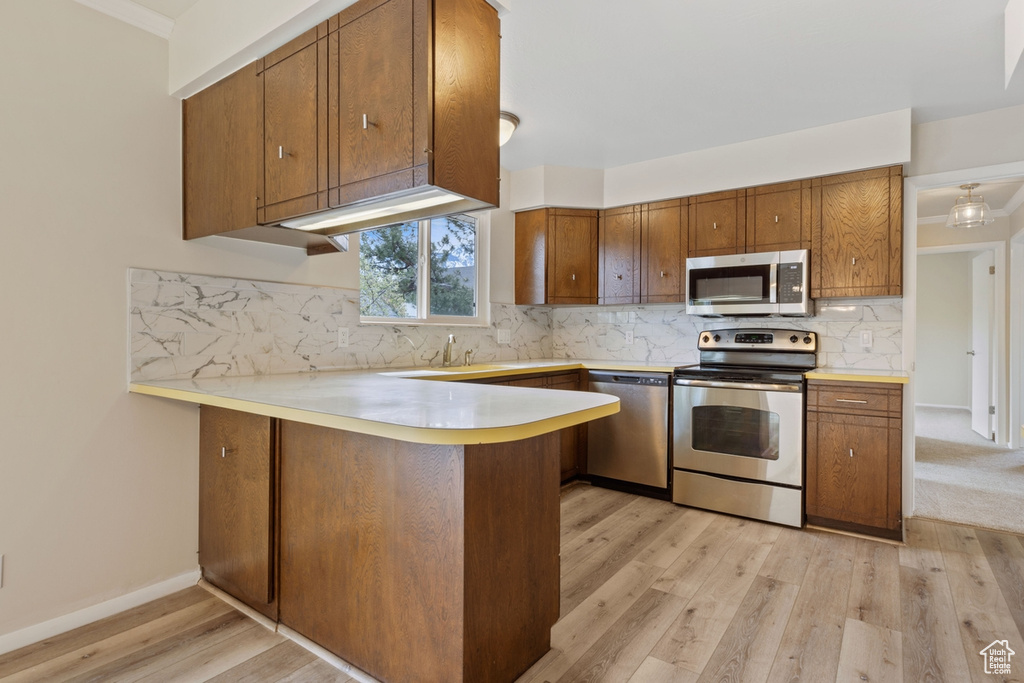 Kitchen featuring kitchen peninsula, appliances with stainless steel finishes, light hardwood / wood-style flooring, backsplash, and sink