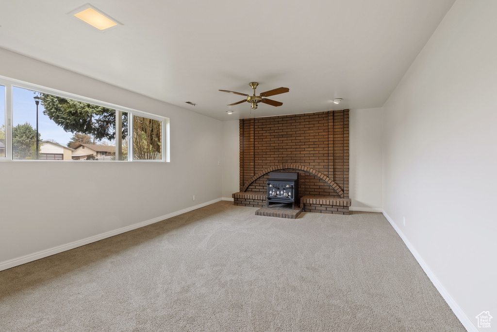 Unfurnished living room featuring carpet floors, ceiling fan, brick wall, and a brick fireplace