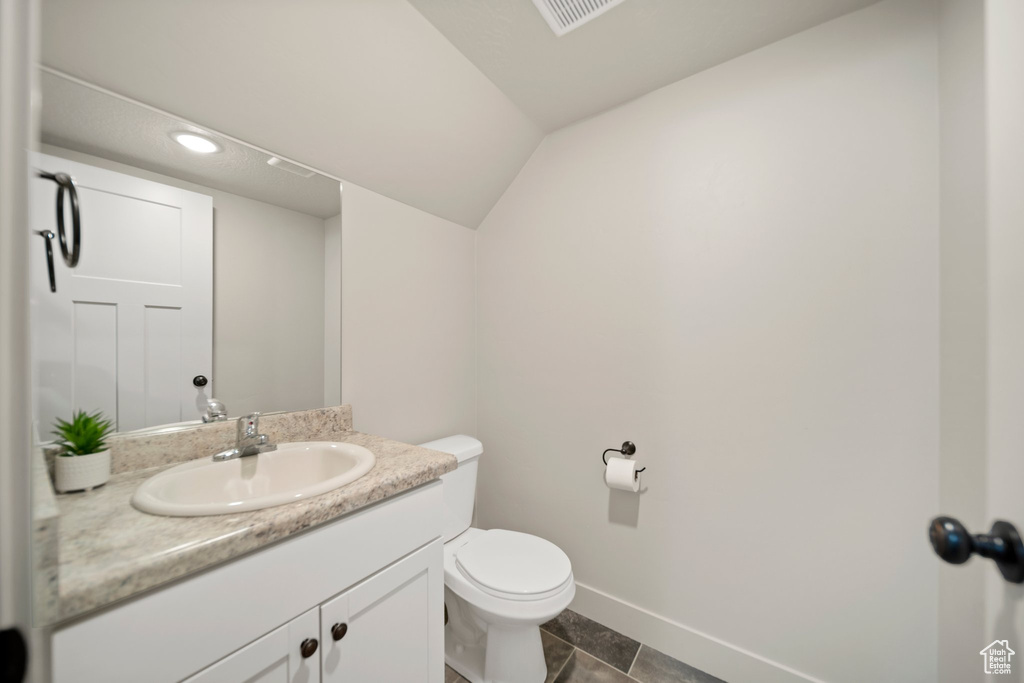 Bathroom featuring toilet, tile flooring, vanity, and lofted ceiling