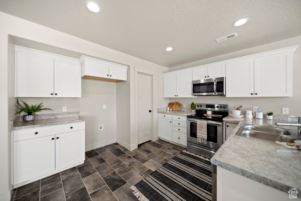 Kitchen with white cabinets, sink, stainless steel appliances, and dark tile flooring