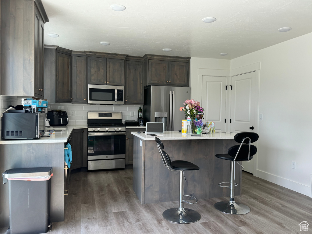 Kitchen featuring stainless steel appliances, tasteful backsplash, hardwood / wood-style floors, dark brown cabinetry, and a center island