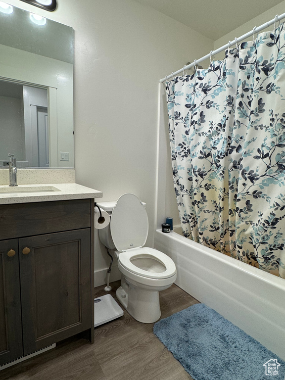 Full bathroom featuring hardwood / wood-style flooring, shower / bathtub combination with curtain, toilet, and large vanity