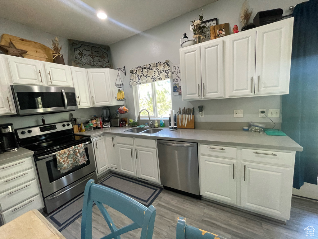 Kitchen featuring white cabinets, sink, wood-type flooring, and stainless steel appliances