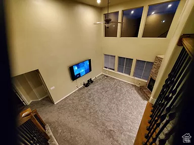 Living room with ceiling fan, carpet, and a towering ceiling