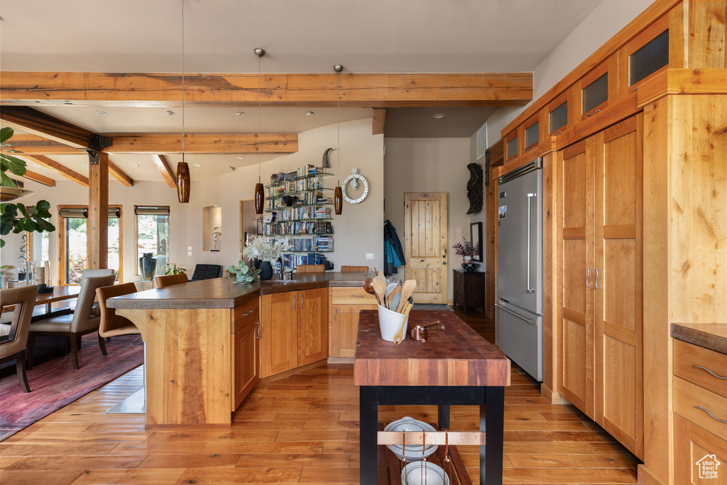 Kitchen with a center island, lofted ceiling with beams, decorative light fixtures, stainless steel built in refrigerator, and light hardwood / wood-style flooring