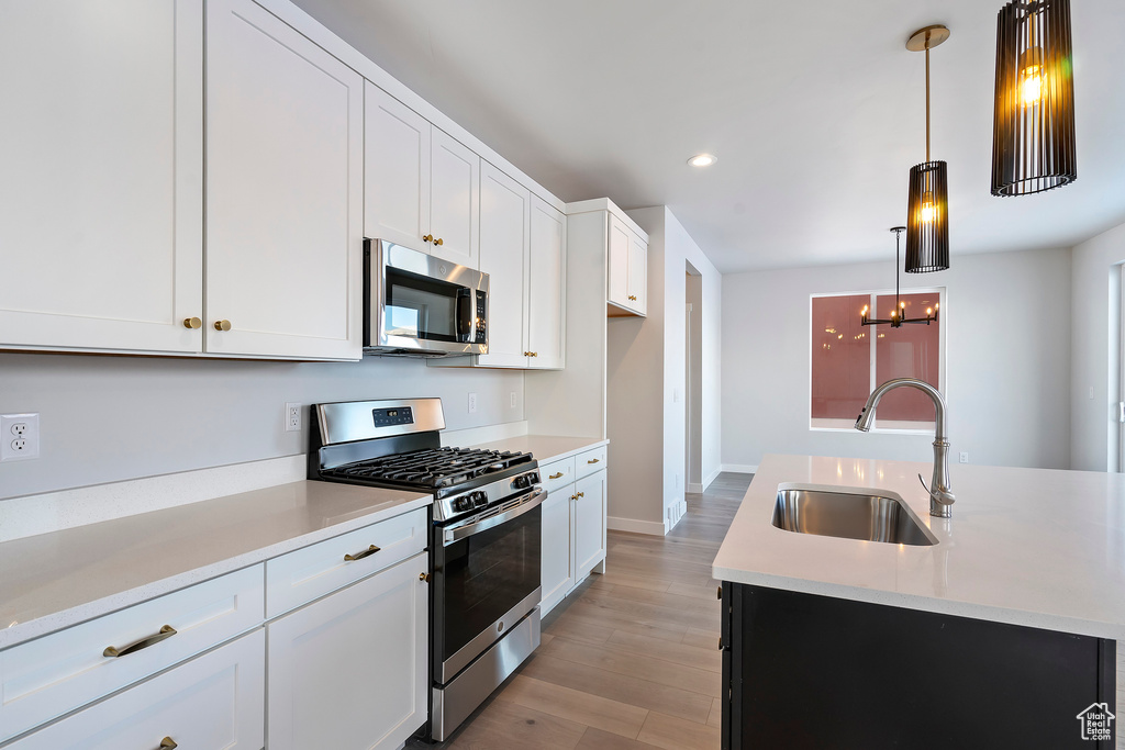 Kitchen featuring appliances with stainless steel finishes, white cabinets, sink, decorative light fixtures, and light hardwood / wood-style flooring