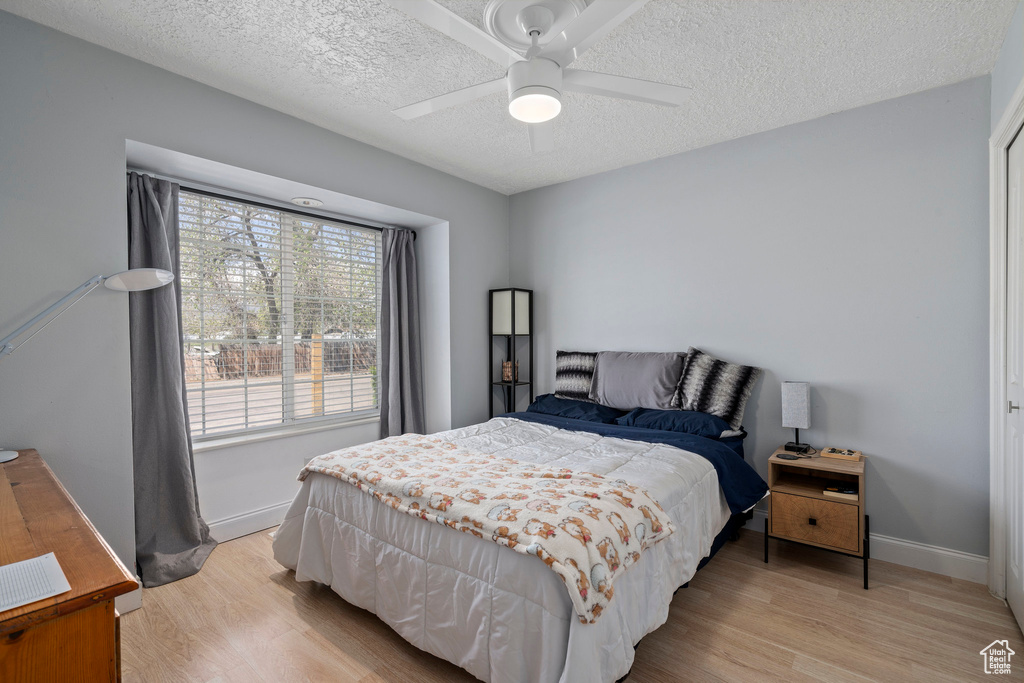 Bedroom with light hardwood / wood-style flooring, ceiling fan, and a textured ceiling