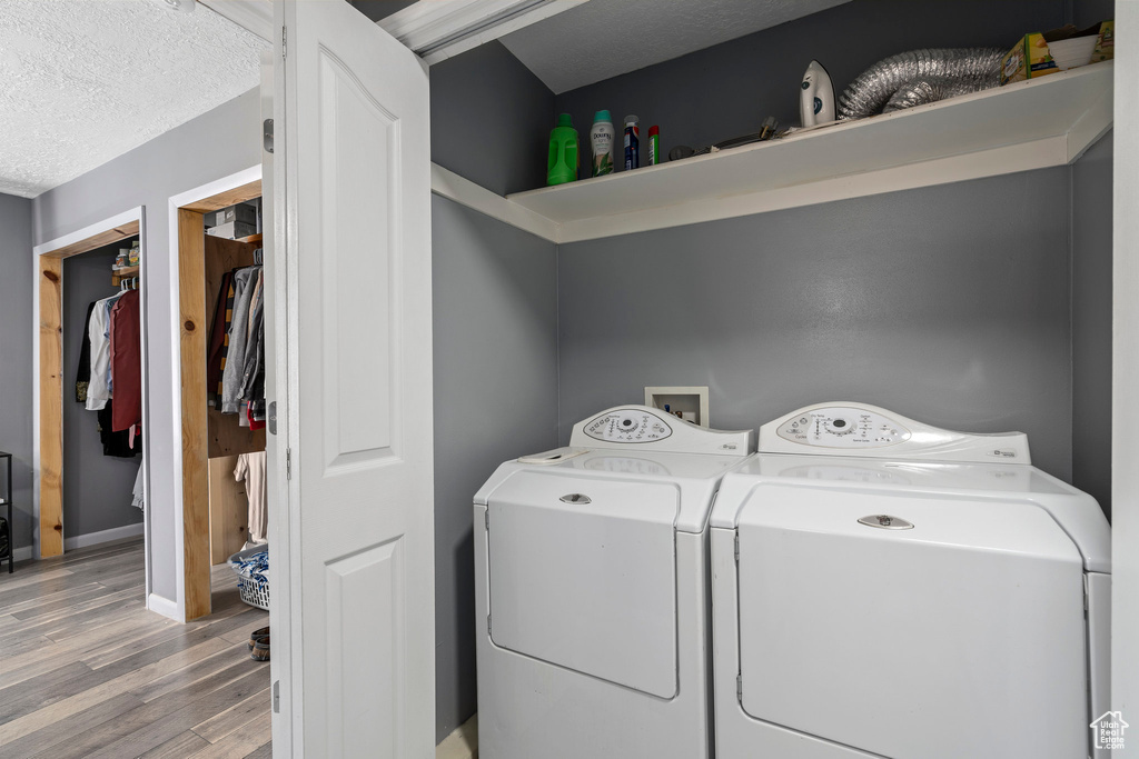 Clothes washing area with hookup for a washing machine, light hardwood / wood-style floors, a textured ceiling, and washer and dryer