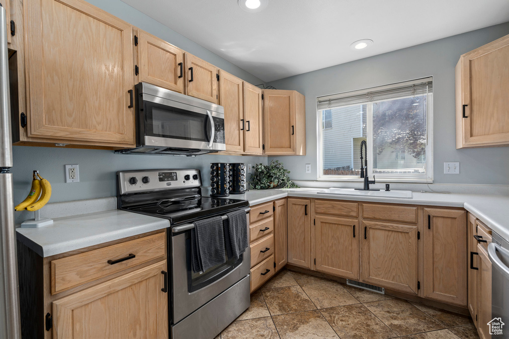 Kitchen featuring appliances with stainless steel finishes, light brown cabinetry, sink, and light tile floors