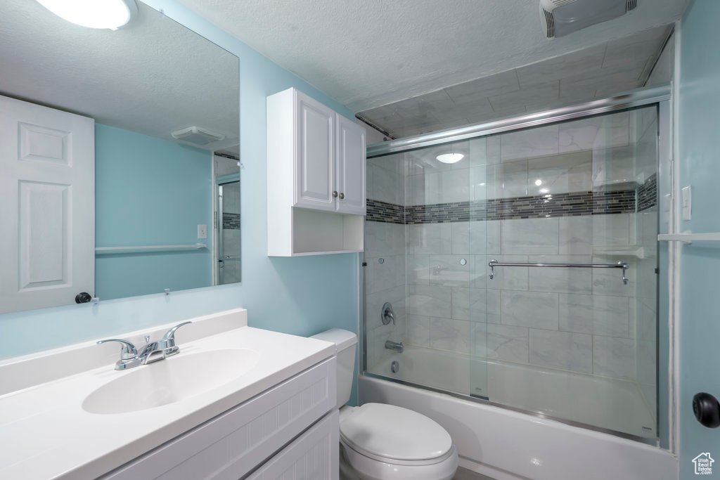 Full bathroom featuring a textured ceiling, vanity, toilet, and enclosed tub / shower combo