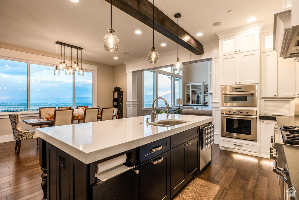 Kitchen with beamed ceiling, white cabinets, sink, decorative light fixtures, and dark hardwood / wood-style floors