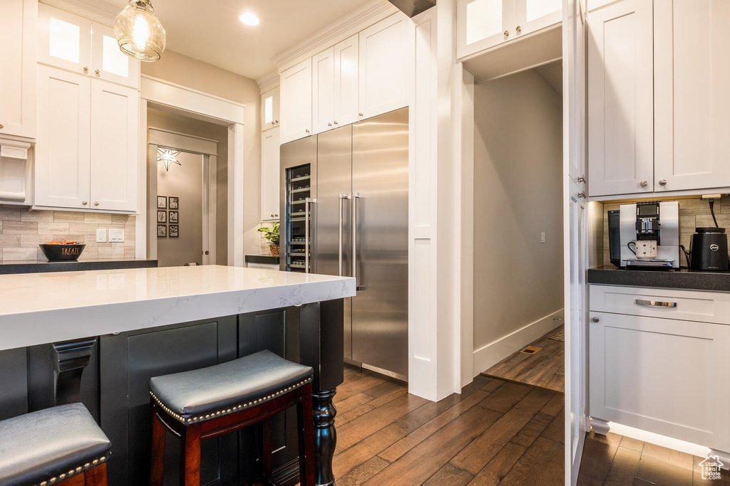 Kitchen with white cabinets, tasteful backsplash, dark wood-type flooring, stainless steel built in refrigerator, and pendant lighting