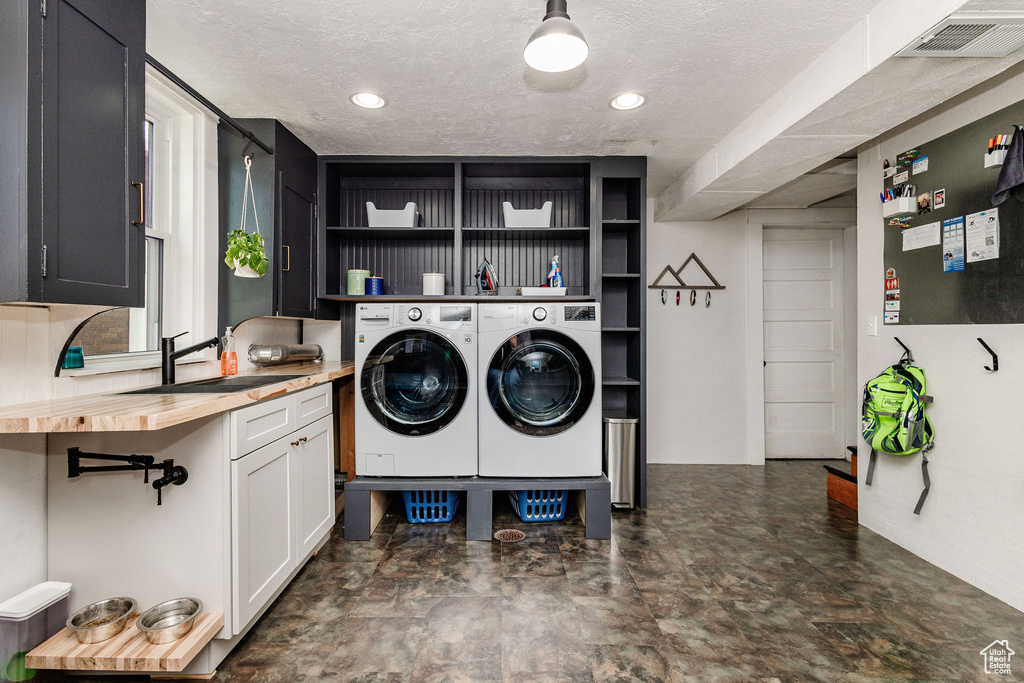Laundry area featuring a textured ceiling, sink, dark tile floors, and washing machine and clothes dryer