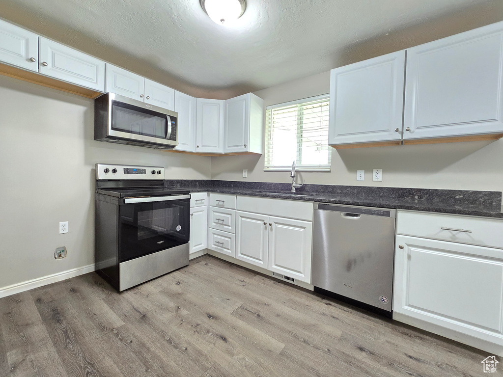 Kitchen featuring appliances with stainless steel finishes, light hardwood / wood-style flooring, sink, and white cabinetry