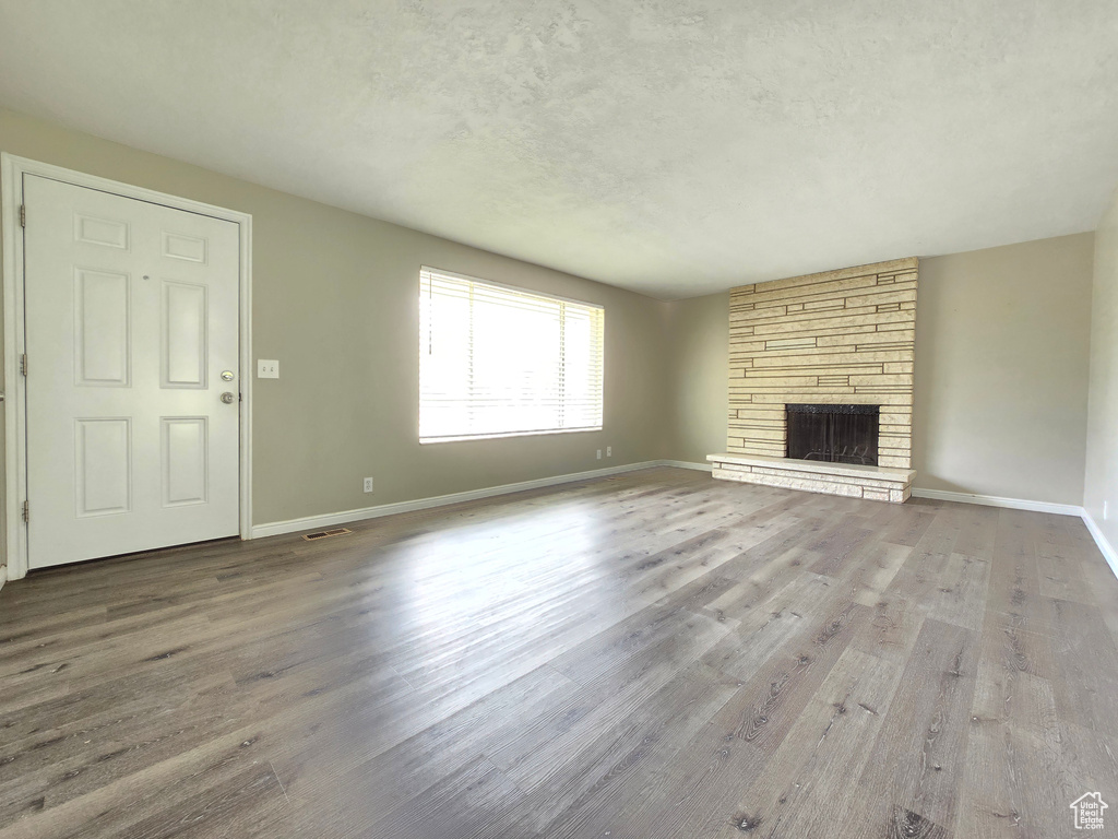 Unfurnished living room featuring a stone fireplace, hardwood / wood-style flooring, and a textured ceiling