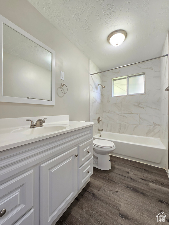 Full bathroom featuring tiled shower / bath, large vanity, a textured ceiling, hardwood / wood-style floors, and toilet