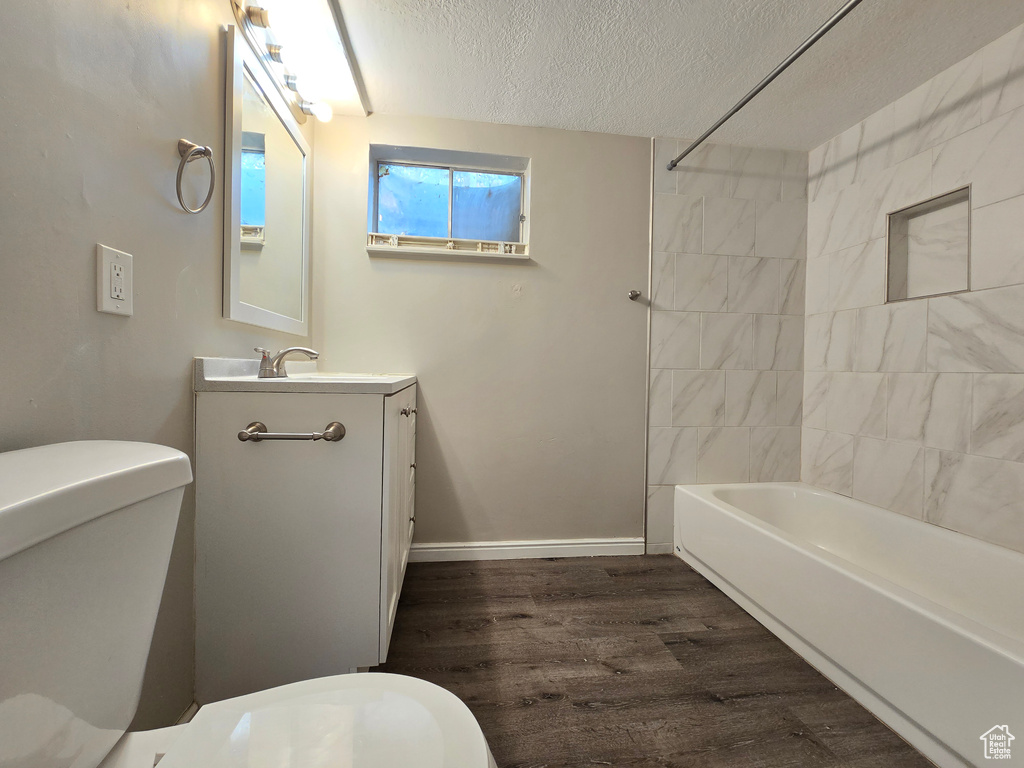 Full bathroom with tiled shower / bath, hardwood / wood-style floors, oversized vanity, toilet, and a textured ceiling